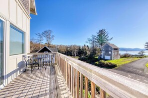 A wooden deck with outdoor furniture, a stone building, and a view of a body of water and mountains. - Spacious Homey Dog Friendly House with Fireplace and Beach and Ocean Views (Netarts)