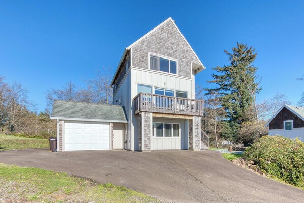 A two-story house with a garage, a balcony, and a driveway. - Spacious Homey Dog Friendly House with Fireplace and Beach and Ocean Views (Netarts)