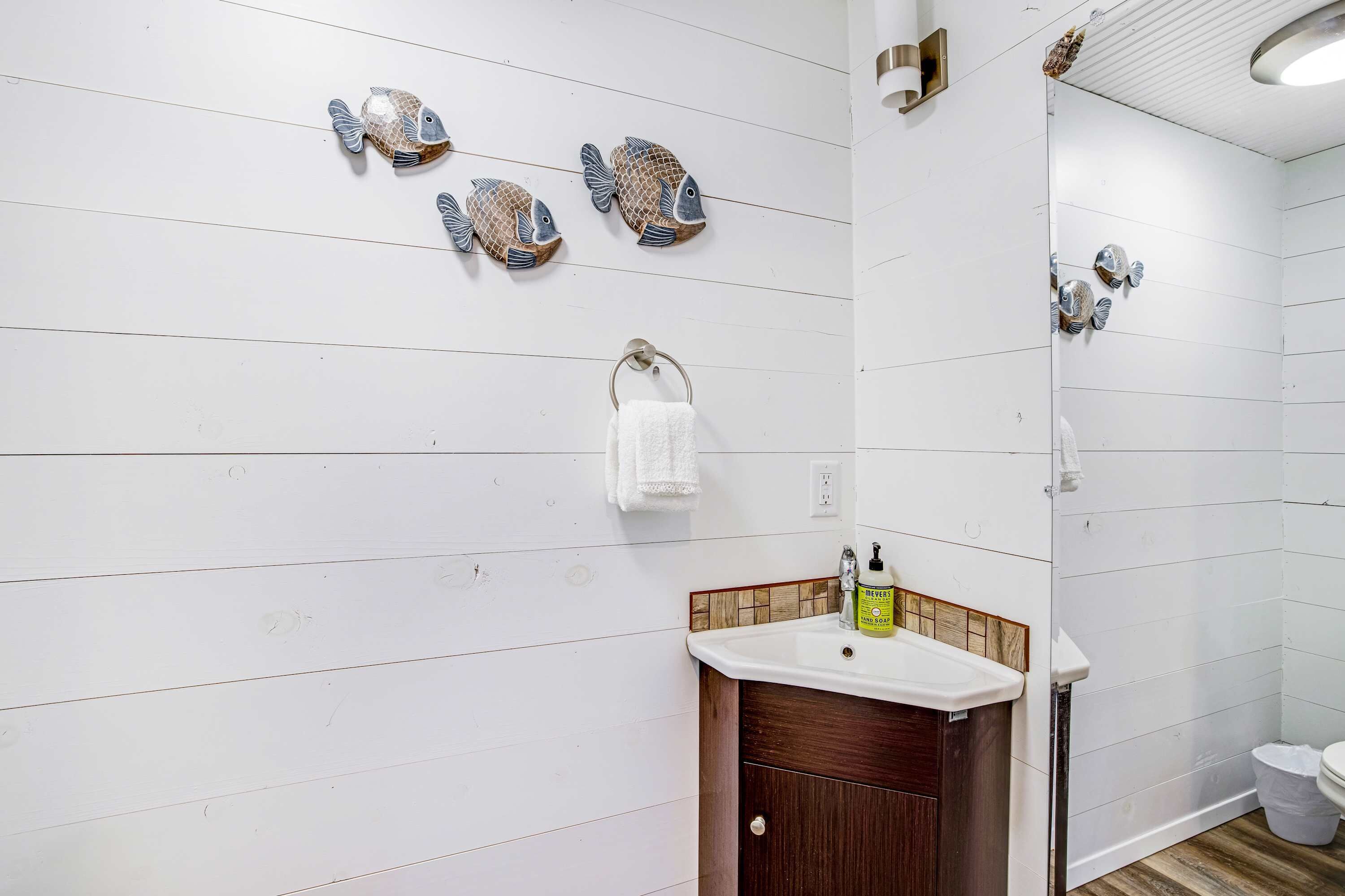 Une salle de bain avec des murs en bois peints en blanc, un meuble-lavabo en bois, un évier avec un flacon de savon liquide et des décorations murales représentant des poissons.