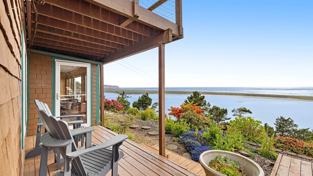 En träveranda med Adirondack-stolar, en krukväxt och utsikt över havet.