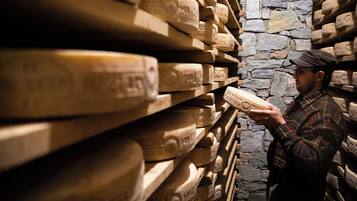A person examining cheese wheels in a cellar with stone walls.