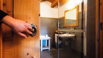 A wooden door with a hand turning a key. Inside, there is a bathroom with a sink, mirror, and a small white table.