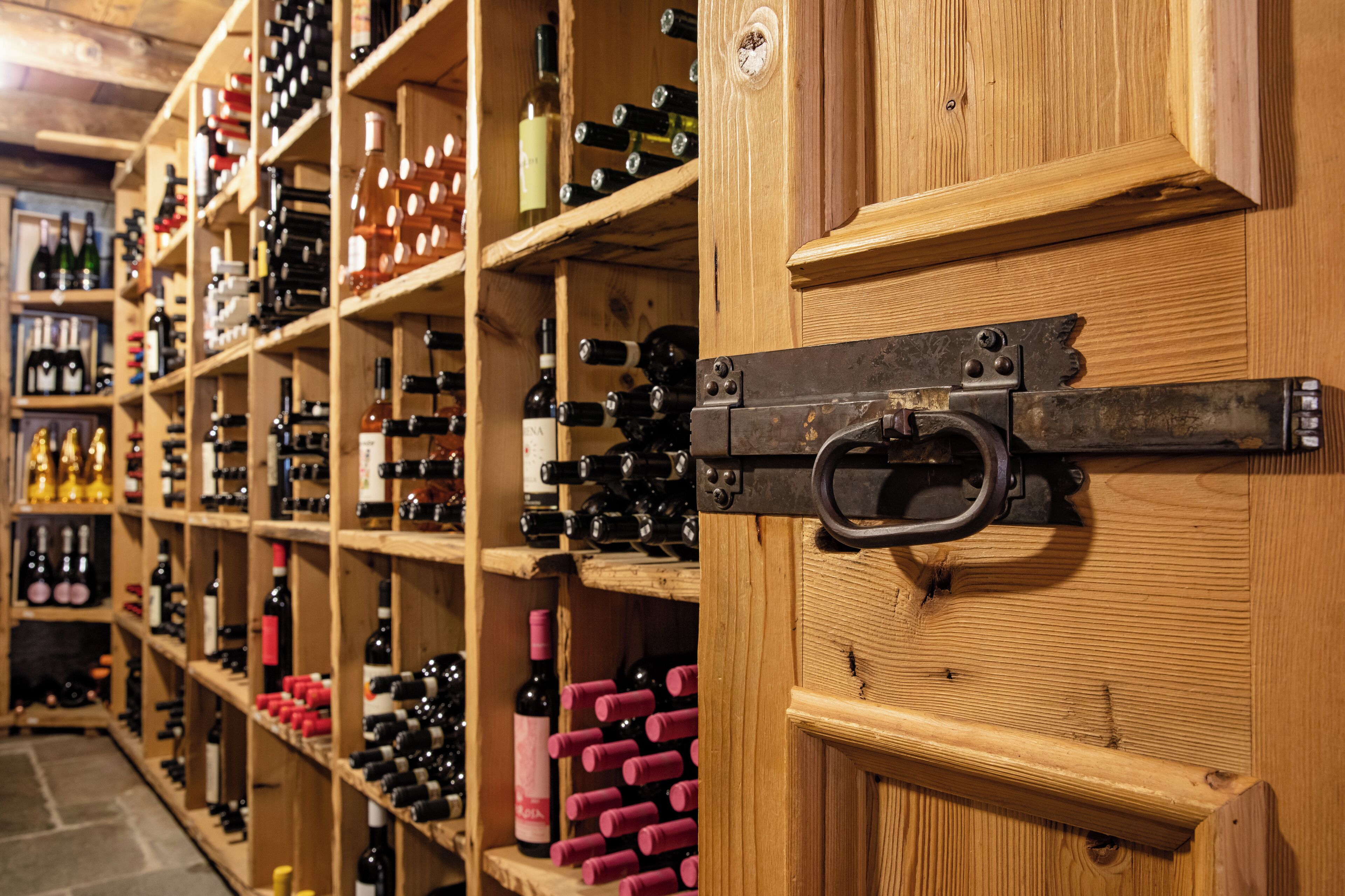 A wine cellar with wooden shelves stocked with various bottles of wine.
