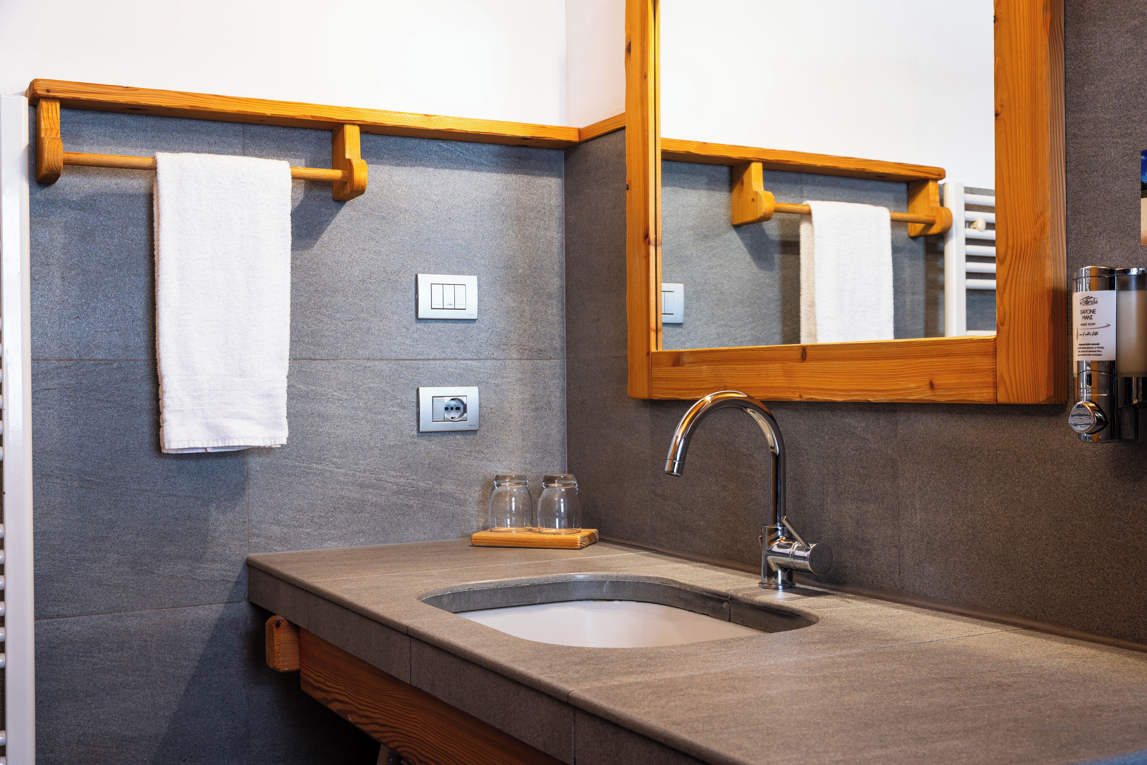 Un baño con lavamanos, espejo, perchero para toallas y dos interruptores de luz.