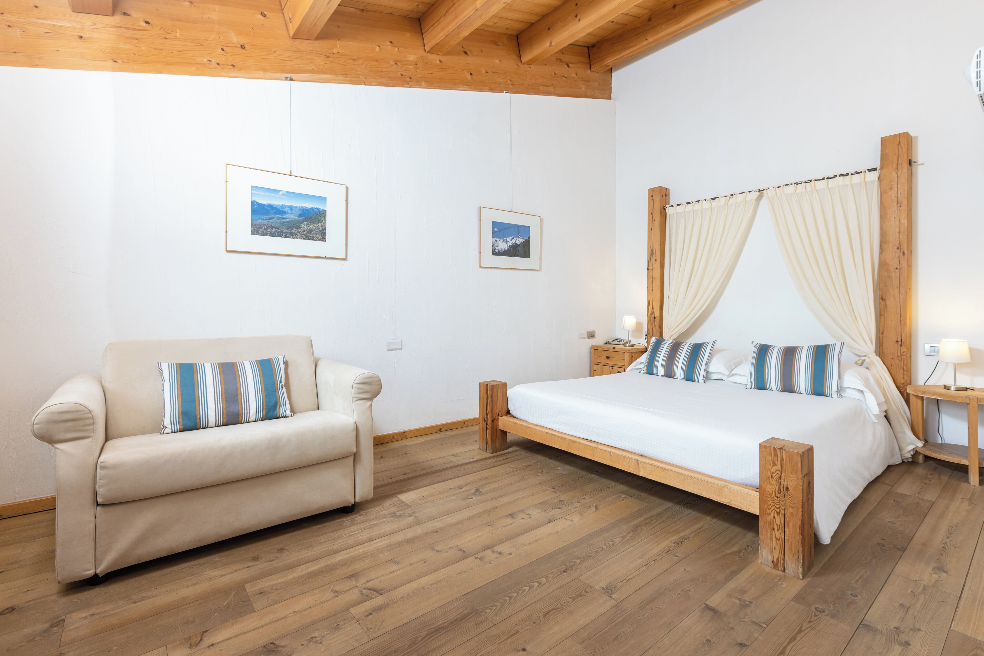 Een slaapkamer met een houten bed, een bank en twee ingelijste foto’s aan de muur.