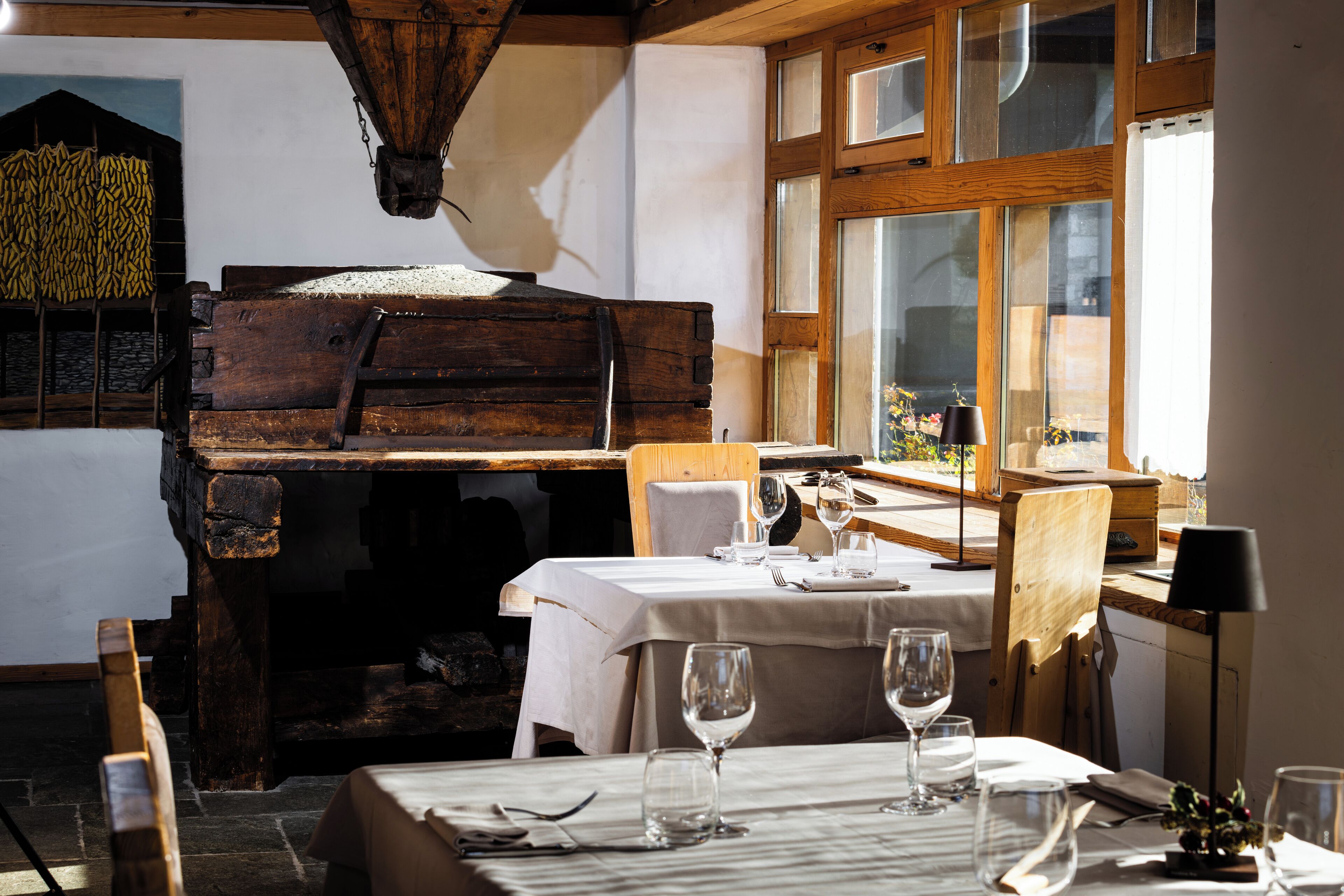 A rustic dining area with wooden furniture, a table set for two, and a large window with natural light.