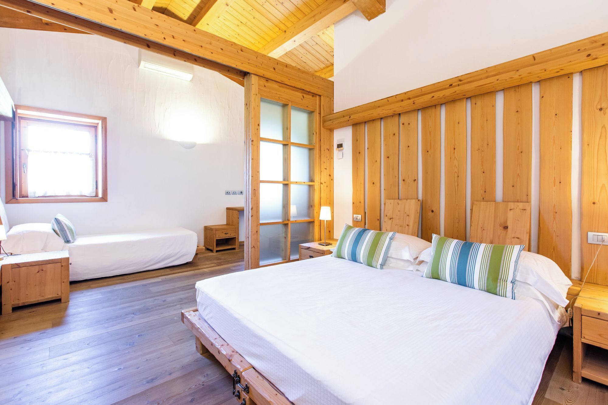 A wooden-paneled bedroom with a large bed, a smaller bed, and a window.