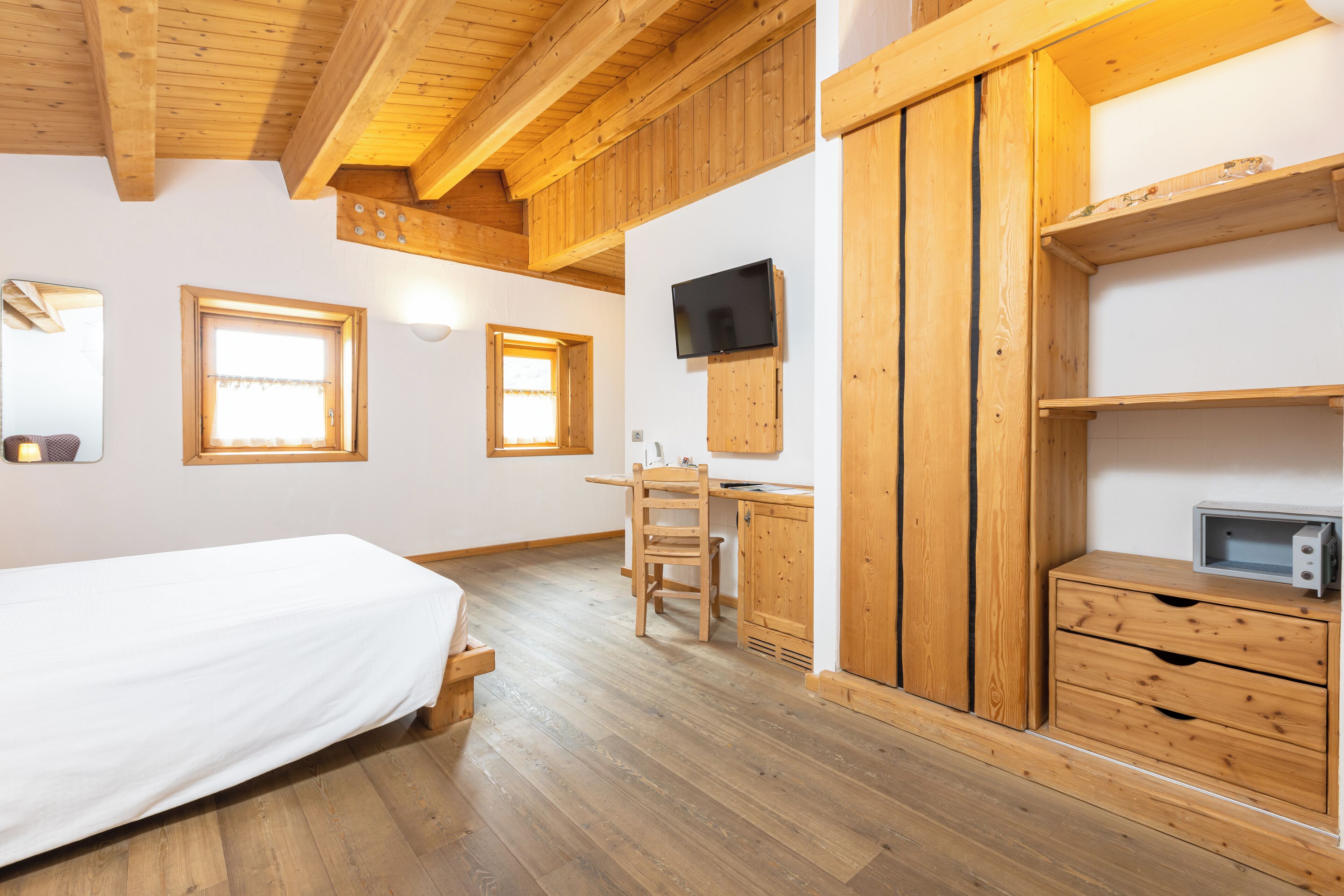 A wooden-floored bedroom with a bed, a desk, and a TV mounted on the wall.