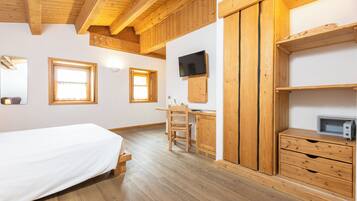 A wooden-floored bedroom with a bed, a desk, and a TV mounted on the wall.