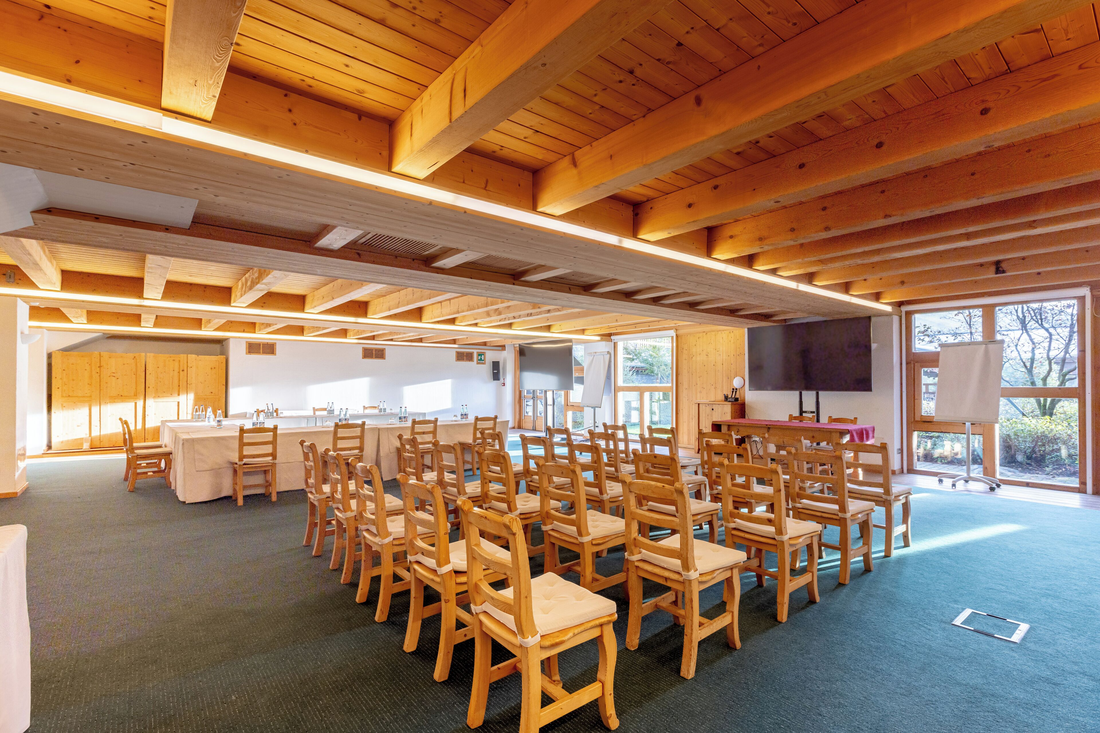 Une salle de conférence dotée de chaises et de tables en bois, de grandes fenêtres et d’un écran de projection.
