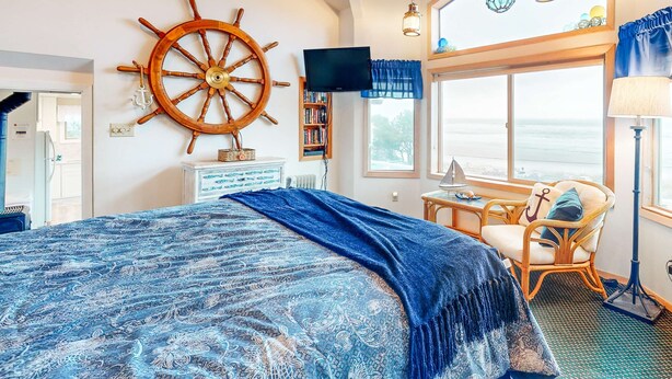 Una camera da letto con un grande letto, una decorazione a muro con una ruota di legno, una televisione, una libreria, una finestra vista e una poltrona in vimini.