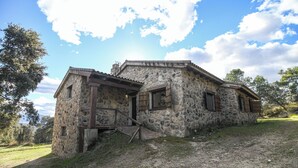A stone building with a wooden staircase leading to a door, surrounded by trees and a clear sky. - Casa Rural Las Corzas (Casavieja)