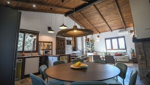 A spacious living area with a wooden ceiling, a dining table with chairs, a kitchen area, and a fireplace. - Casa Rural Las Corzas (Casavieja)