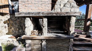 A stone-built outdoor grill with a brick wall backdrop, a wooden bench, and a stone ledge with firewood. - Casa Rural Las Corzas (Casavieja)