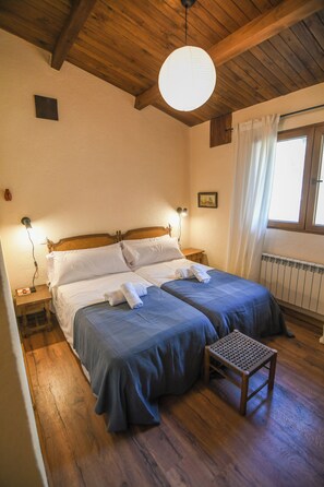 A room with two beds, wooden flooring, a small table, and a ceiling light. - Casa Rural Las Corzas (Casavieja)