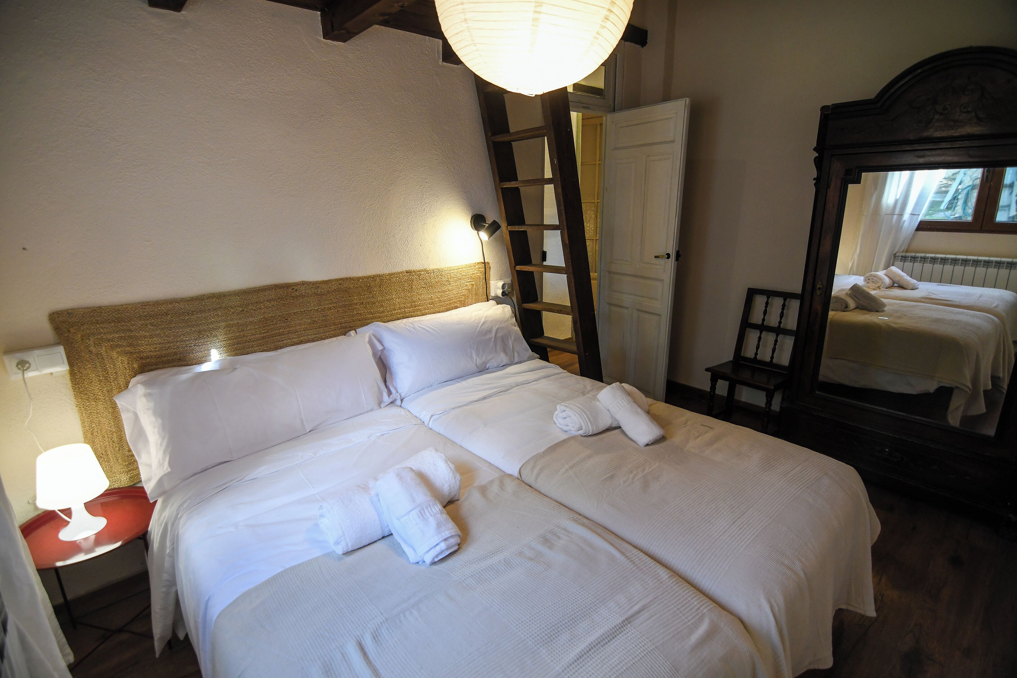 Ein ordentlich gemachtes Bett mit weißen Leinen und Handtüchern, eine Holzleiter, ein Spiegel und eine Lampe auf einem Nachttisch.