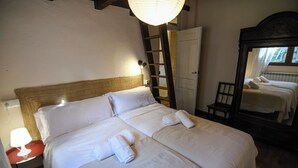 A neatly made bed with white linens and towels, a wooden ladder, a mirror, and a lamp on a nightstand.