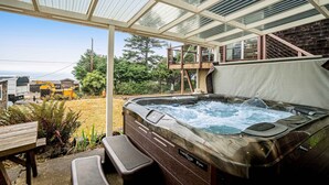 A hot tub in a covered outdoor area with a view of a yard and a building in the background.