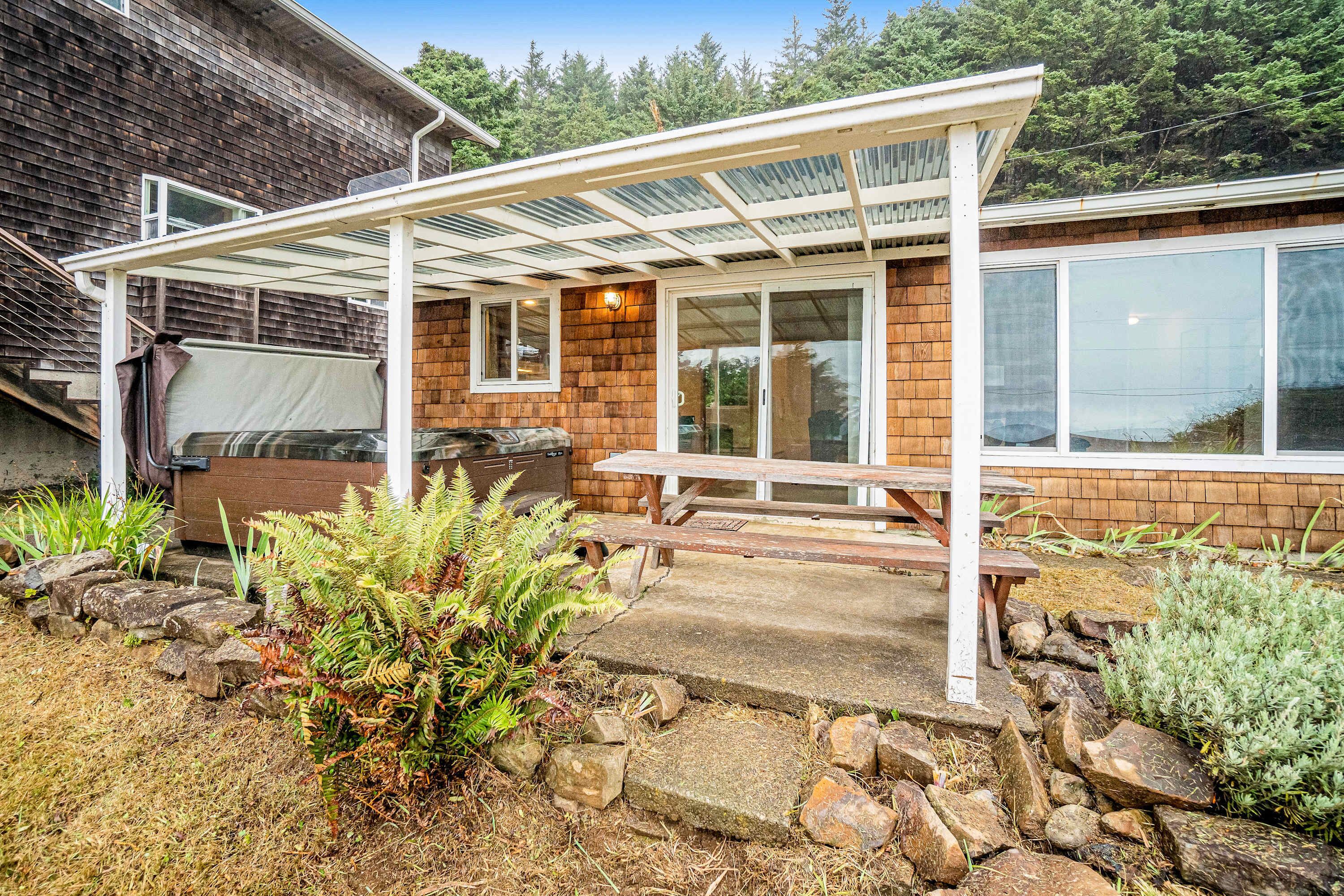 A covered patio area with a barbecue grill, picnic table, and stone pathway.
