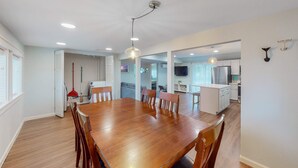 A spacious dining area with a wooden table and chairs, a ceiling light fixture, and a view into the kitchen area.