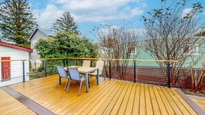 A wooden deck with a table and chairs, surrounded by a metal fence and trees.