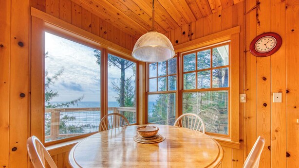 Ein Esszimmer aus Holz mit einem runden Tisch, Stühlen, einer Pendelleuchte und großen Fenstern mit Blick ins Freie.