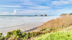 Ein Strand mit blauem Himmel, ruhigem Wasser und zwei markanten Felsen in der Ferne.