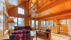 Eine geräumige Holzhütte mit Schlafzimmer im oberen Bereich, einem gemütlichen Wohnbereich mit Sofa und Esstisch sowie einer Küche mit Holzschränken.