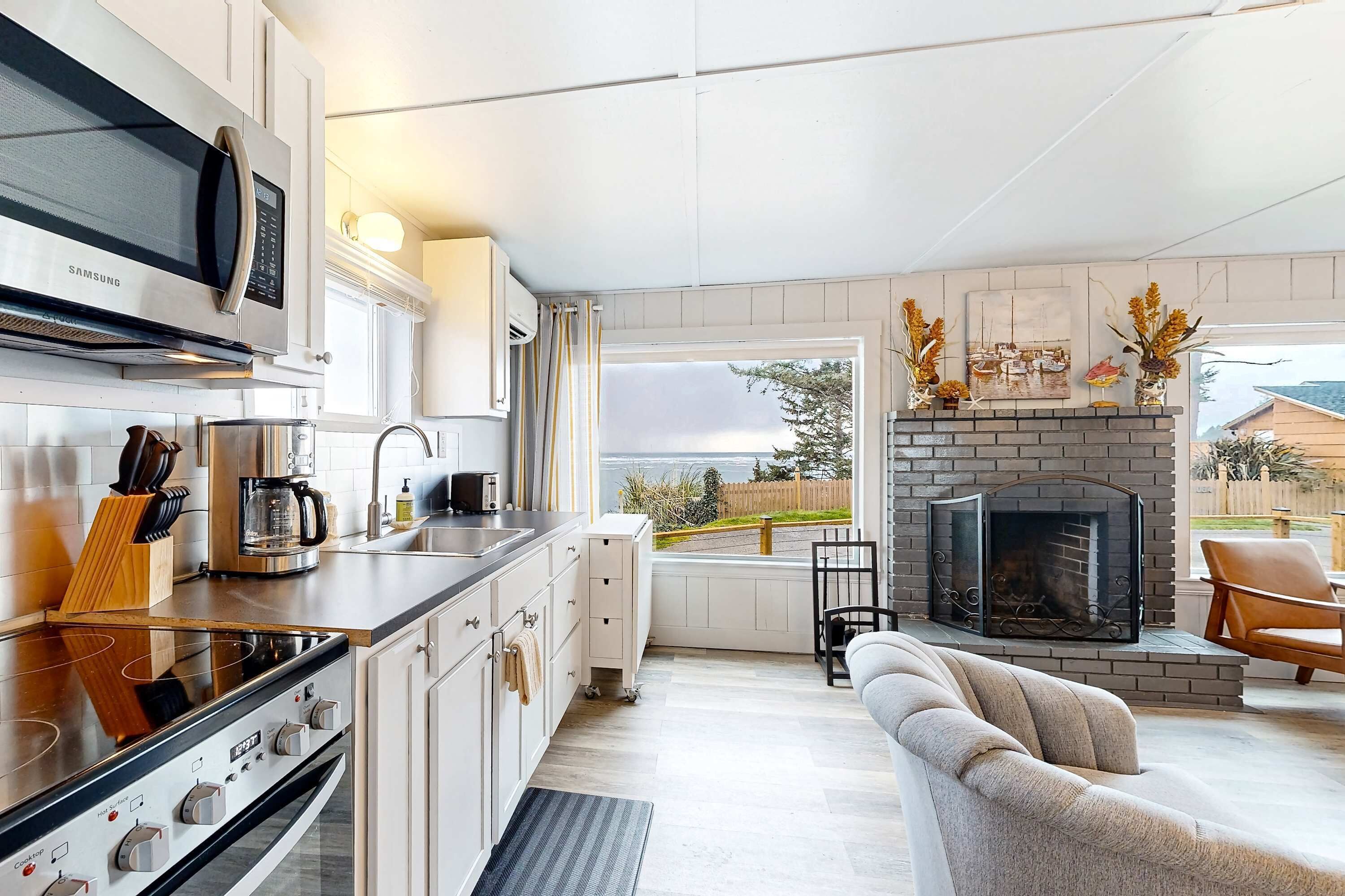 A modern kitchen with a built-in microwave, stove, and coffee maker. There is a fireplace with decorative items and a view of the outside.