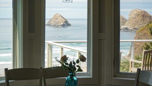 Habitación con un amplio ventanal que ofrece vistas al océano y acantilados rocosos. Hay una mesa de madera con un jarrón de flores en el centro.