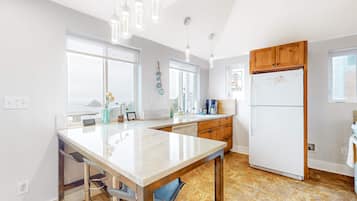 A kitchen with a marble countertop, wooden cabinets, a white refrigerator, and pendant lighting.