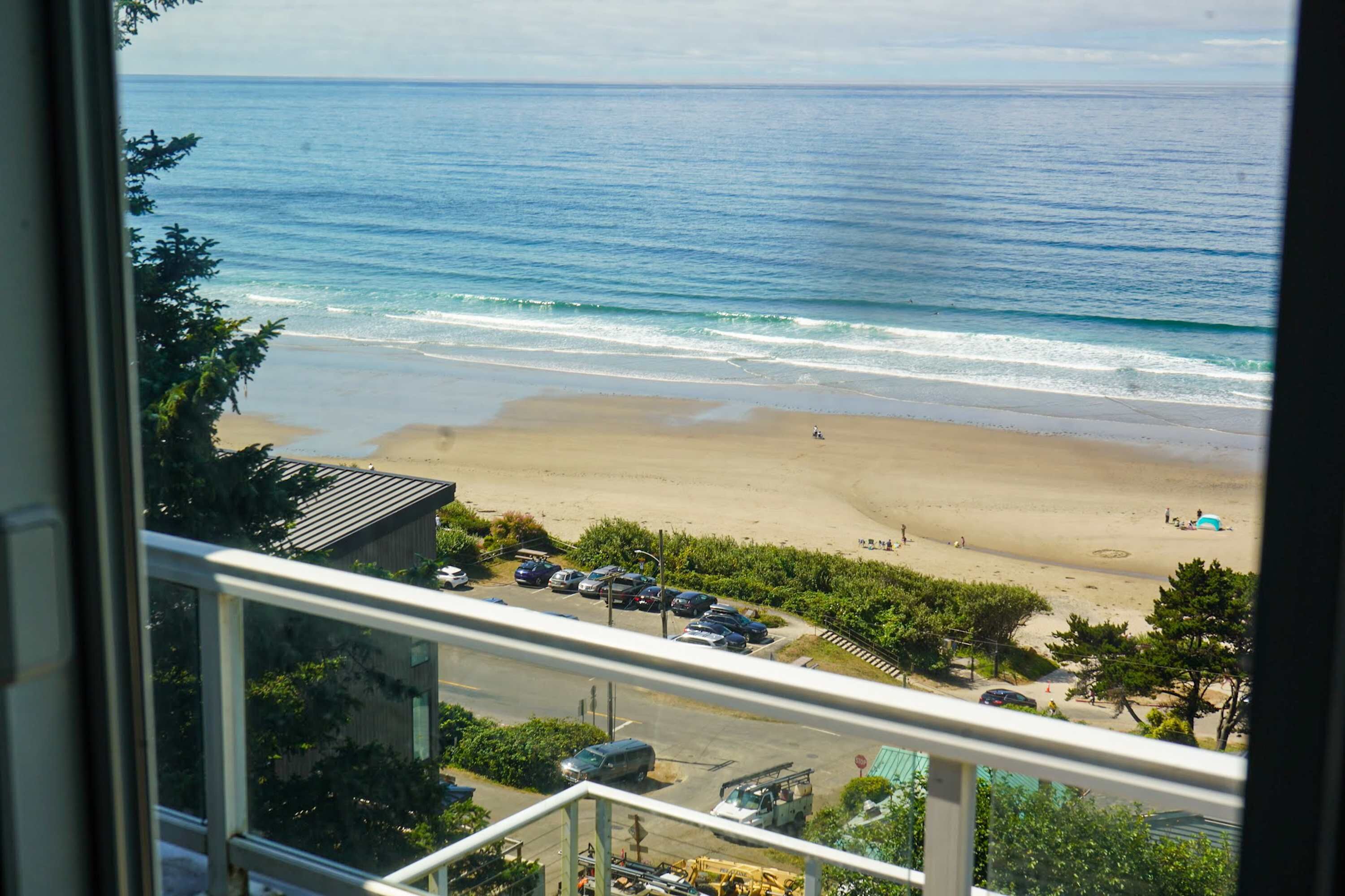 Blick auf den Strand durch ein Fenster, mit Parkplatz, Autos und einigen Personen.