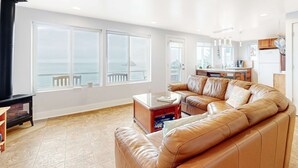 Un salon spacieux, doté d’un grand canapé en cuir, d’une table basse et offrant une vue sur la mer grâce à de grandes fenêtres.