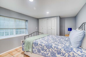 A bedroom with a bed, a window with blinds, a wardrobe, and a nightstand with a lamp. - Downstairs Oceanview Hideout with Sweeping Views and Easy Beach Access (Oceanside)