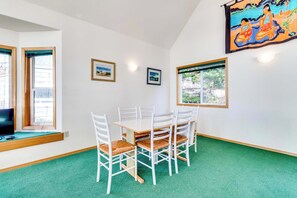Un coin repas avec une table ronde et des chaises blanches, un téléviseur posé sur un rebord de fenêtre et des tableaux encadrés accrochés aux murs.