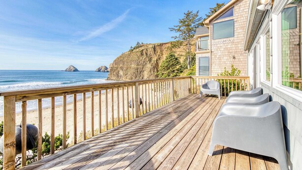 Un terrazza in legno con vista sull'oceano, un edificio con ampie vetrate e posti a sedere all'aperto.