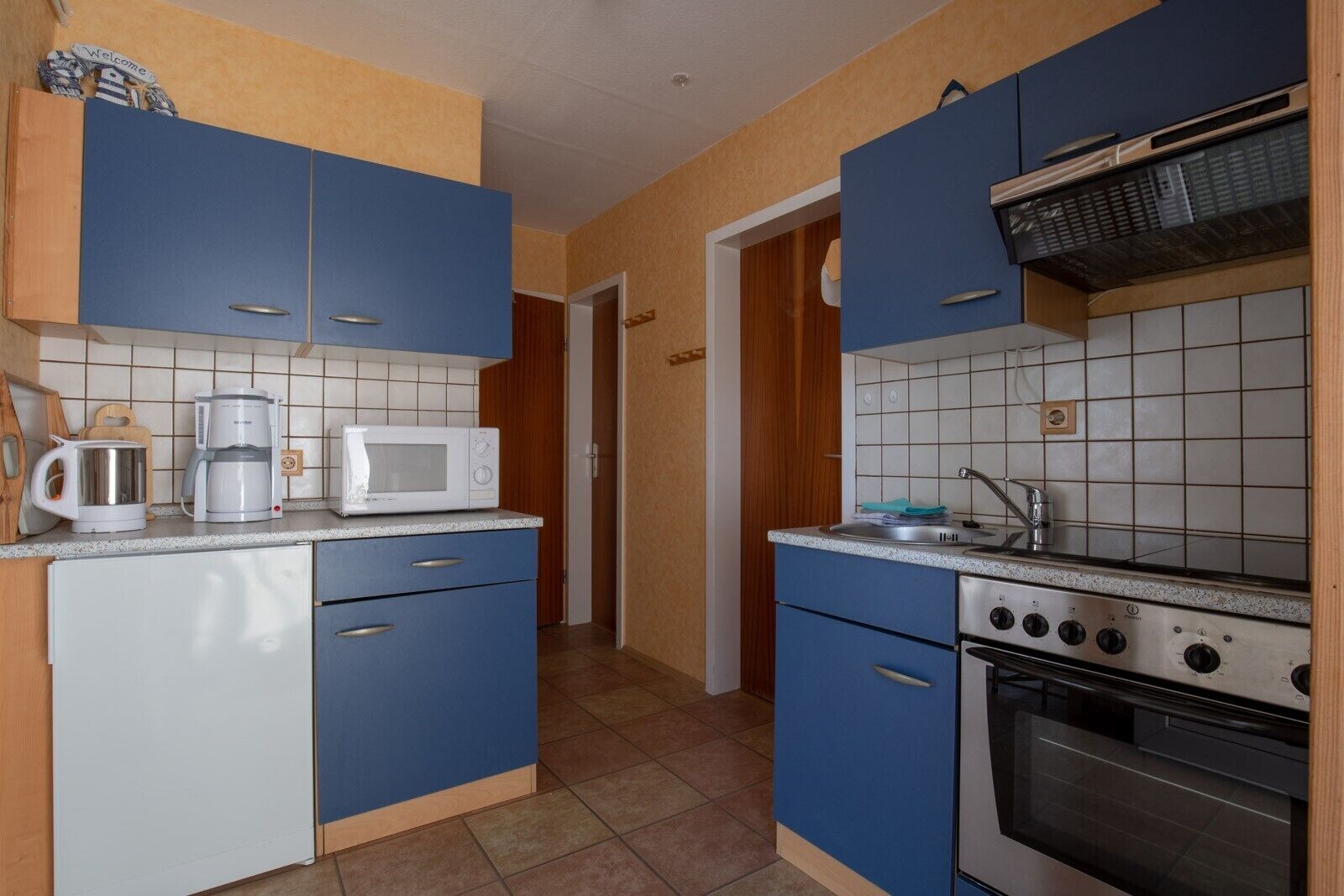 Una cucina compatta con mobili blu, un forno a microonde bianco, una macchina da caffè e un piano cottura.