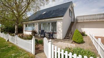 Ein eingeschossiges Haus mit Terrasse, weißem Zaun und kleinem Garten.
