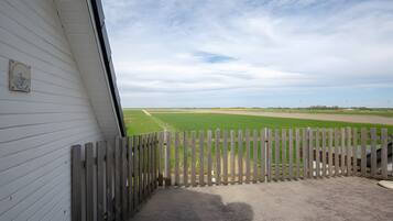 Blick durch einen Holzzaun auf ein grünes Feld, ein weißes Gebäude mit einem Fenster und einem klaren Himmel.