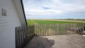 A view through a wooden fence to a green field, a white building with a window, and a clear sky. - Wattenläuper Holiday Apartment (Pellworm)