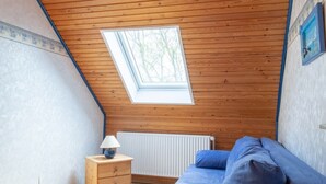 A room with a sloped ceiling, a skylight, a bed with blue bedding, a small wooden nightstand, and a radiator. - Wattenläuper Holiday Apartment (Pellworm)