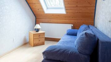 Ein Zimmer mit schräg steilendem Dach, einem Oberlicht, einem Bett mit blauer Bettwäsche, einem kleinen Nachttisch aus Holz und einer Heizung.
