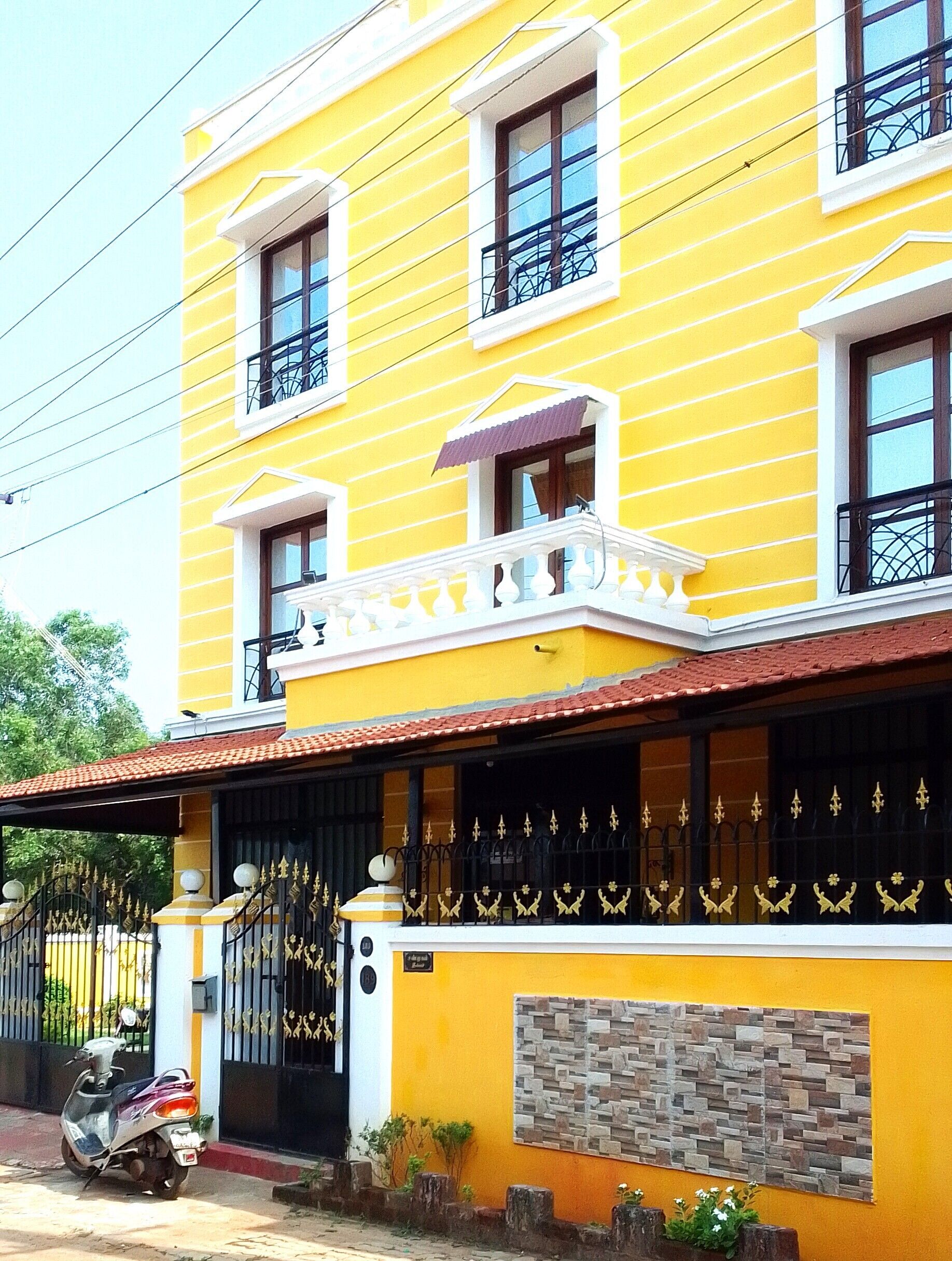 A yellow building with a balcony, a gated entrance, and a scooter parked in front.