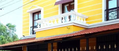 A yellow building with a balcony, a gated entrance, and a scooter parked in front.