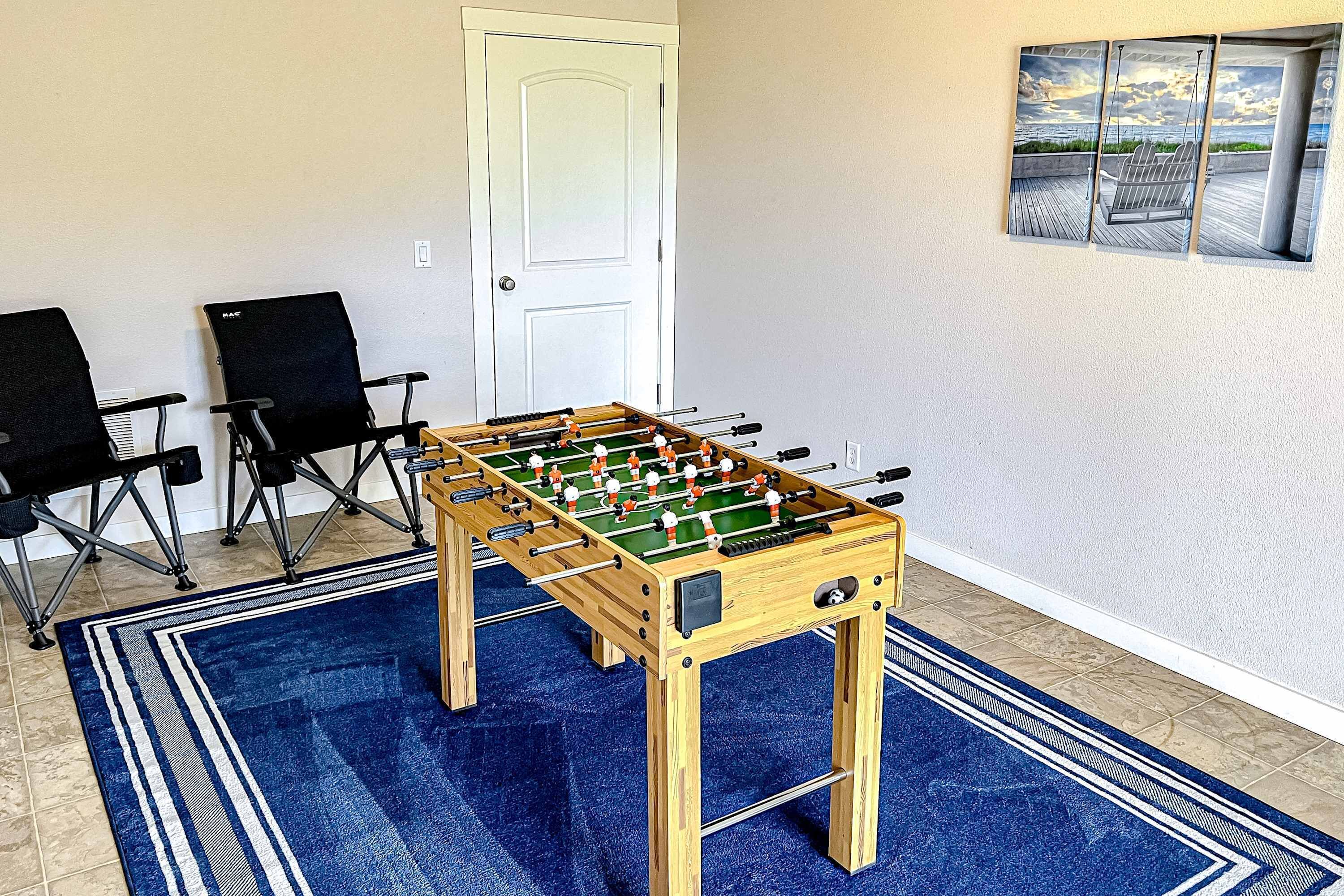 A room with a foosball table, two black chairs, a blue patterned rug, and a door.