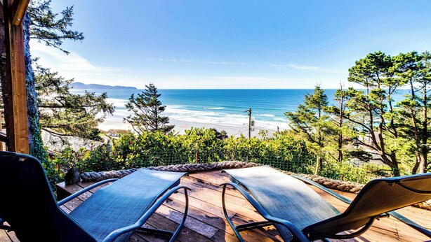 Eine Holzterrasse mit zwei Liegestühlen mit Blick auf einen Strand und das Meer.