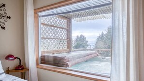 Un dormitorio con un ventanal grande, una cama, una mesita de noche con lámpara y vistas a una piscina y zona exterior.