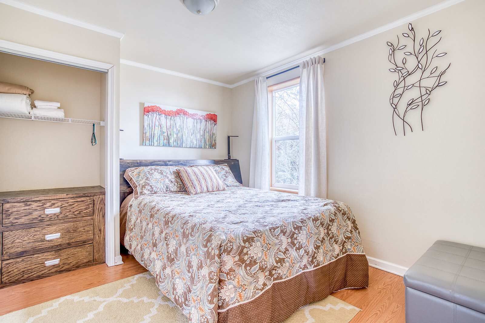 A bedroom with a bed, a dresser, a window with curtains, and a wall art piece.