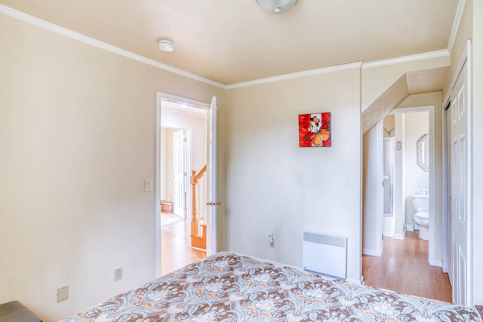 A bedroom with a bed, a door leading to another room, a red artwork on the wall, and a ceiling light.