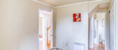 A bedroom with a bed, a door leading to another room, a red artwork on the wall, and a ceiling light.
